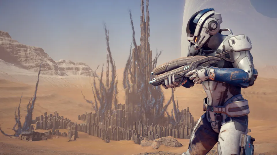An explorer in white armor aims a rifle in front of alien rock towers in Mass Effect: Andromeda