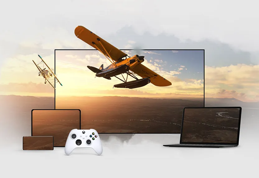A seaplane game streaming on a TV, a laptop and a tablet next to a white Xbox controller