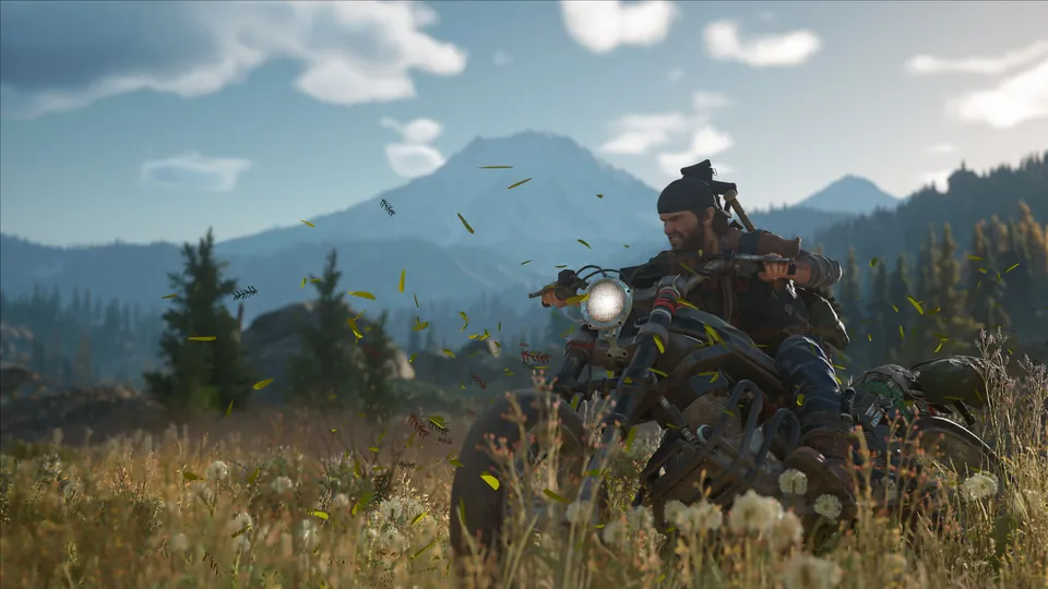 Deacon St. John rides a motorcycle through tall grass with a snowy mountain behind in Days Gone