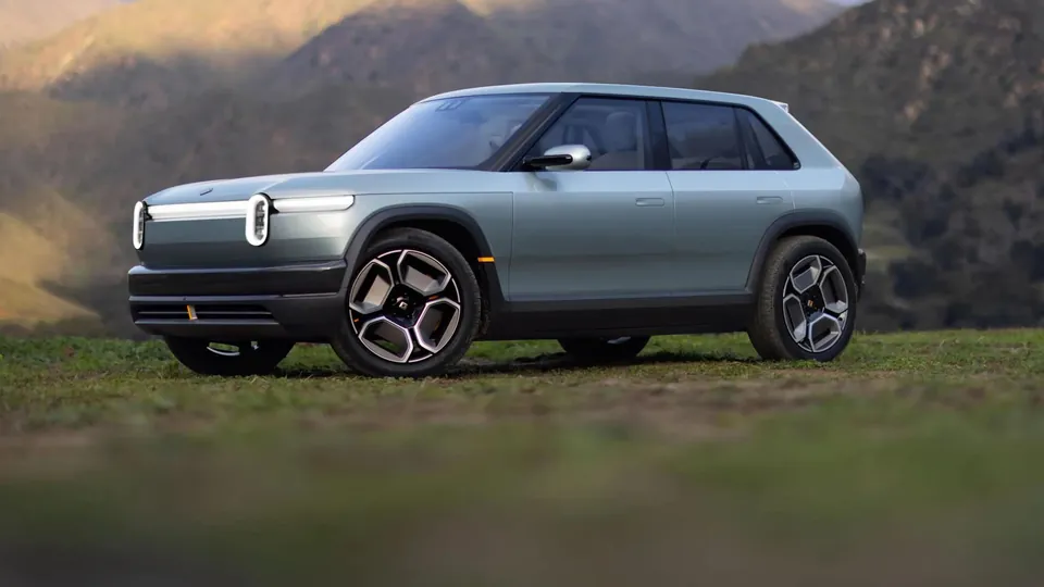 A light green Rivian R3 crossover parked on grass in front of mountains, seen from the front three-quarter angle