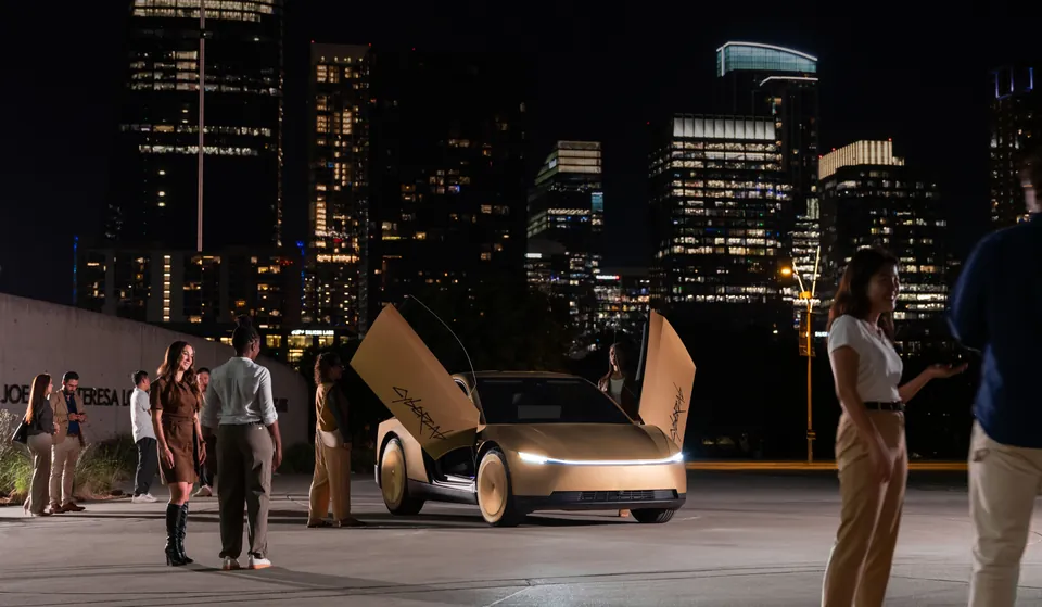 A gold Tesla Cybercab with both doors raised, parked at night