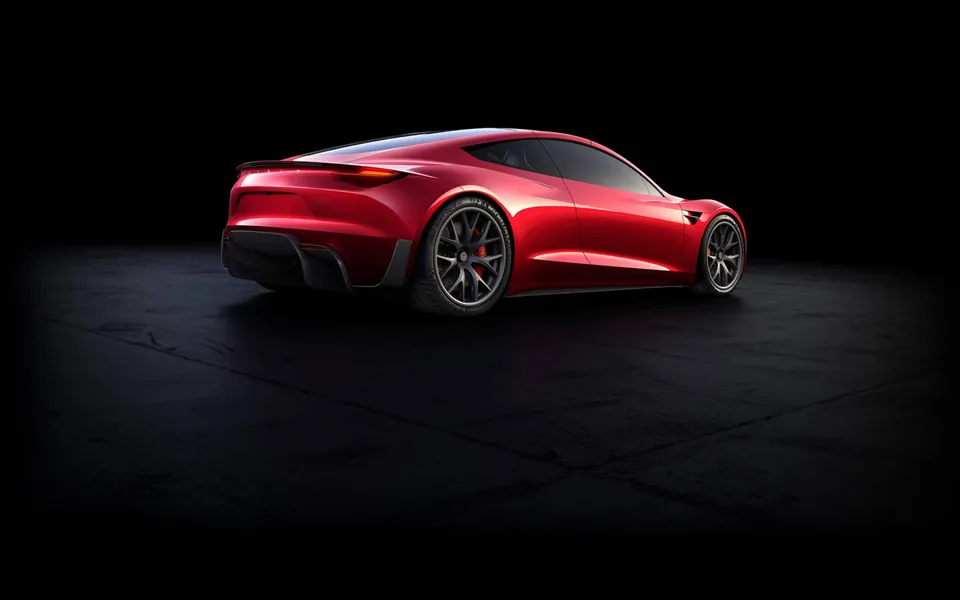 Rear three-quarter view of a red Tesla Roadster prototype on a dark floor