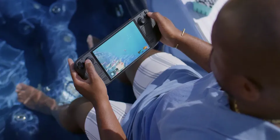 A person in a blue shirt plays a game on a Steam Deck while sitting on a couch