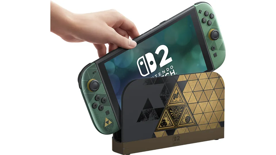A hand sets the Zelda edition Switch 2 with green and gold Joy-Con 2 controllers into its Triforce dock.