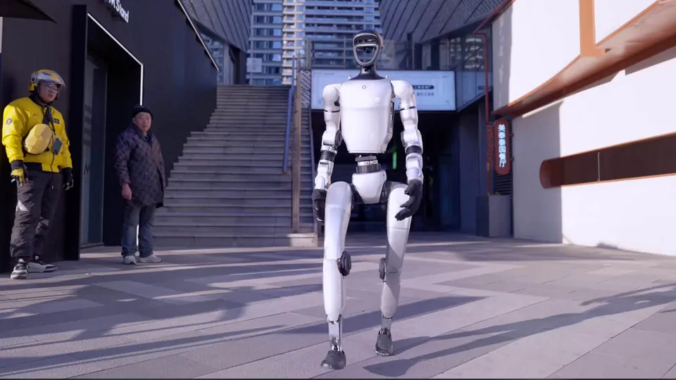 A Unitree G1 walks across a city plaza past two people
