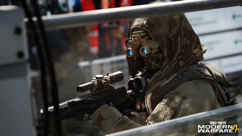 A sniper in a hooded camouflage suit and night-vision goggles aims a scoped rifle