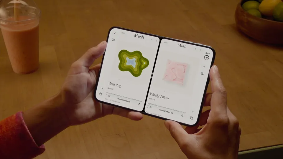 Two hands holding an open iPhone Duo over a table, with two shopping app windows side by side on the inner screen