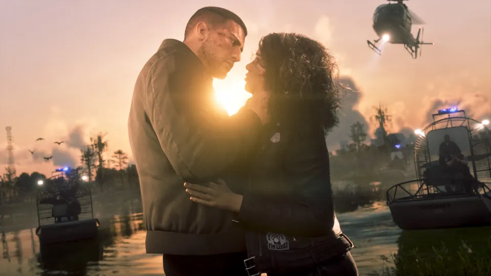 Jason and Lucia embrace at sunset by the water as police airboats and a helicopter close in