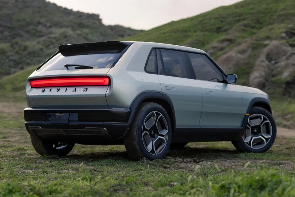 A Rivian R3 seen from the rear on a grassy hillside, with a full-width red taillight