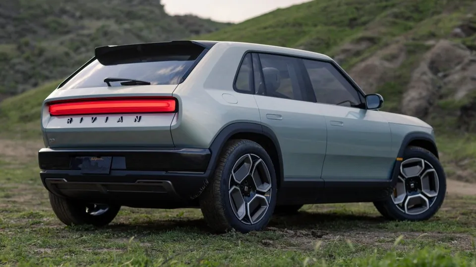 A Rivian R3 seen from the rear on a grassy hillside, with a full-width red taillight