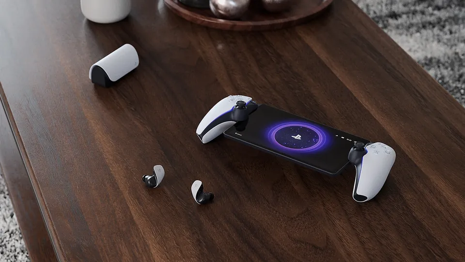 A white PlayStation Portal remote player and wireless earbuds on a wooden coffee table.