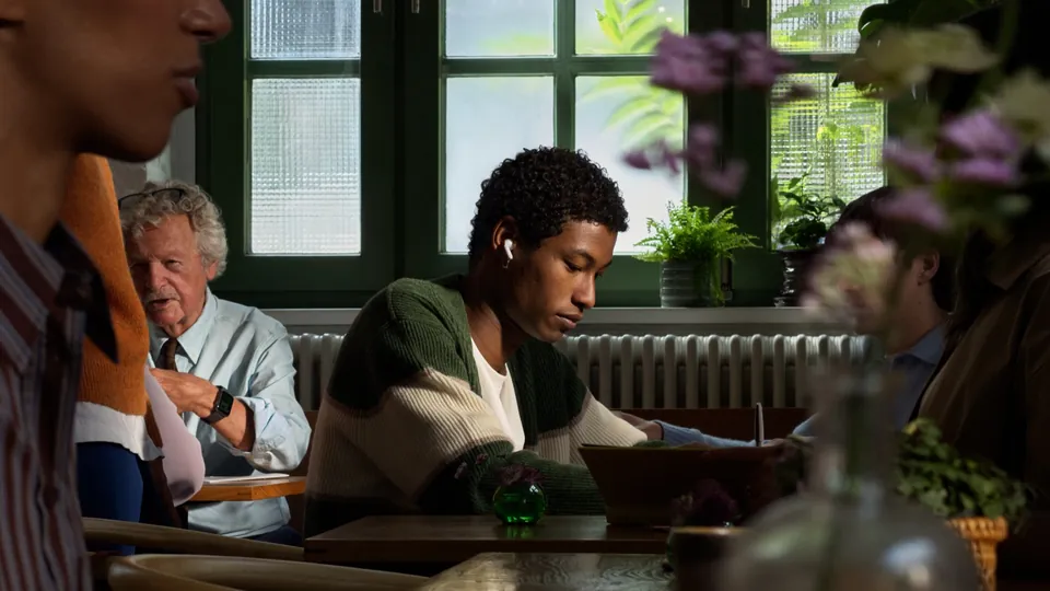 A young man wearing AirPods 5 reads at a cafe table