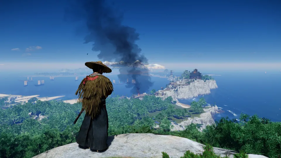 Jin Sakai in a straw cloak looks out over the coast and a burning castle in Ghost of Tsushima