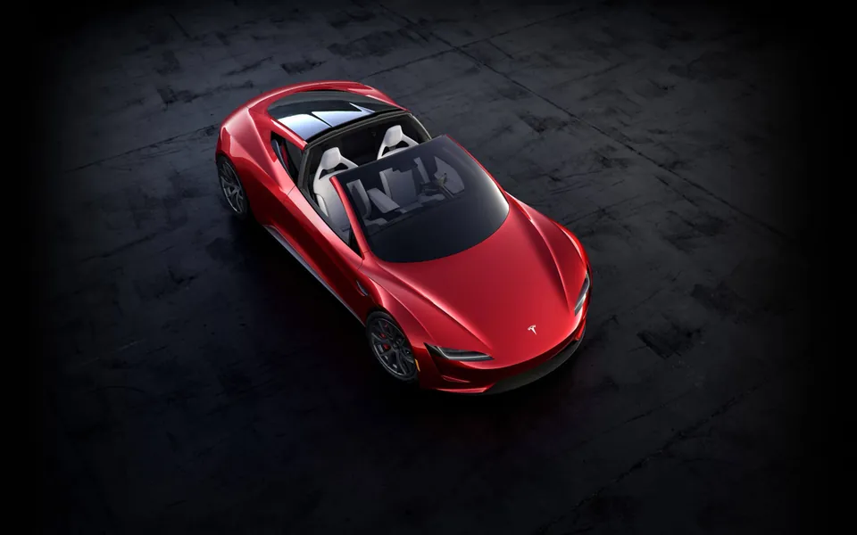 Overhead view of a red Tesla Roadster prototype with its glass roof removed, showing white seats