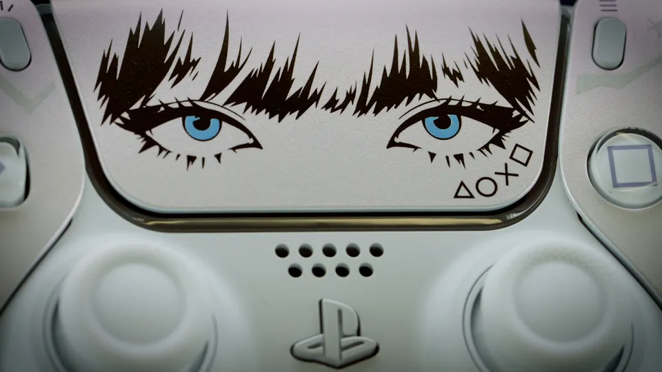 A close-up of the DualSense LISA Limited Edition touch pad with dark bangs, blue eyes and the PlayStation shapes