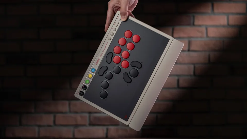 A hand holds the N Edition of the 8BitDo Arcade Controller Pro by one corner against a brick wall, with the wrist rest attached
