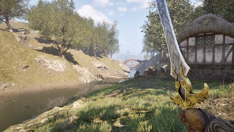 A first-person view of a golden sword raised over a grassy riverbank near a thatched village house