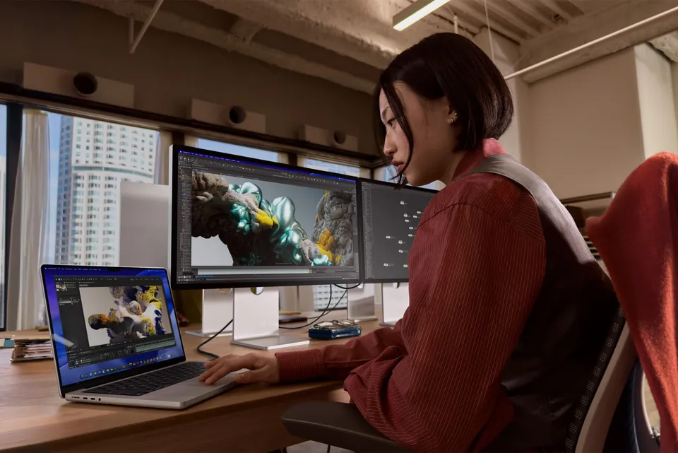 A woman edits video on a MacBook Pro with M5 Pro at a desk with two monitors