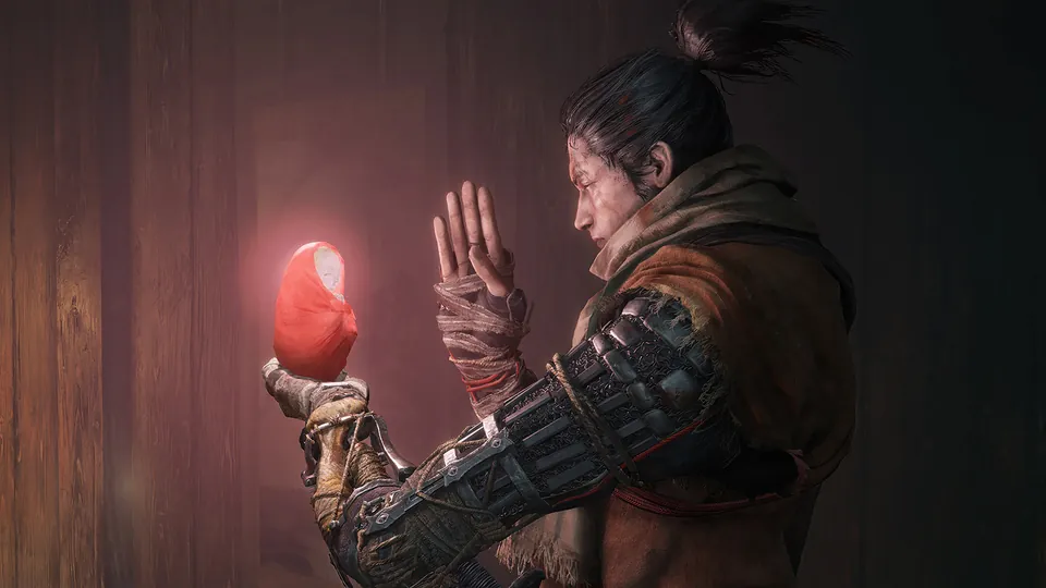 The one-armed shinobi from Sekiro: Shadows Die Twice holds up a small glowing figure wrapped in red cloth in a dark wooden room