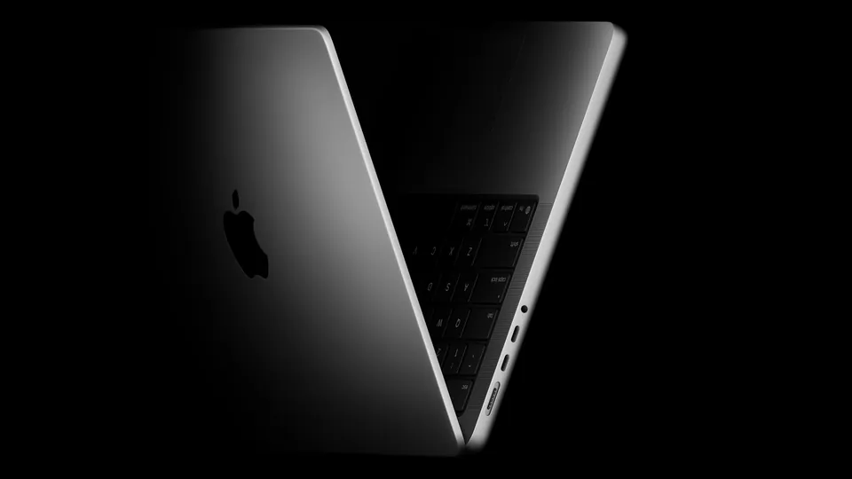 The 14-inch MacBook Pro with M5, half open, seen from the side in the dark