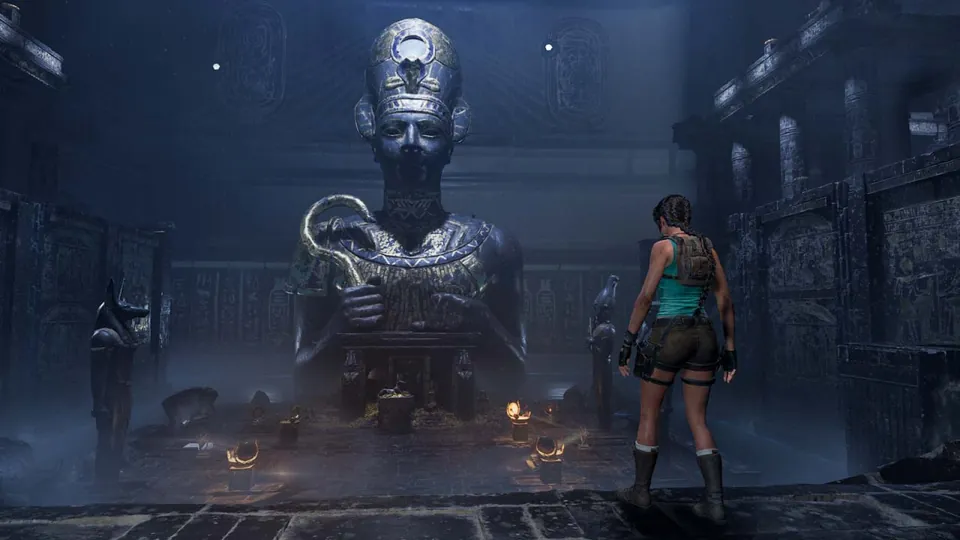Lara Croft stands before a giant pharaoh statue in a dark Egyptian tomb in Tomb Raider: Legacy of Atlantis