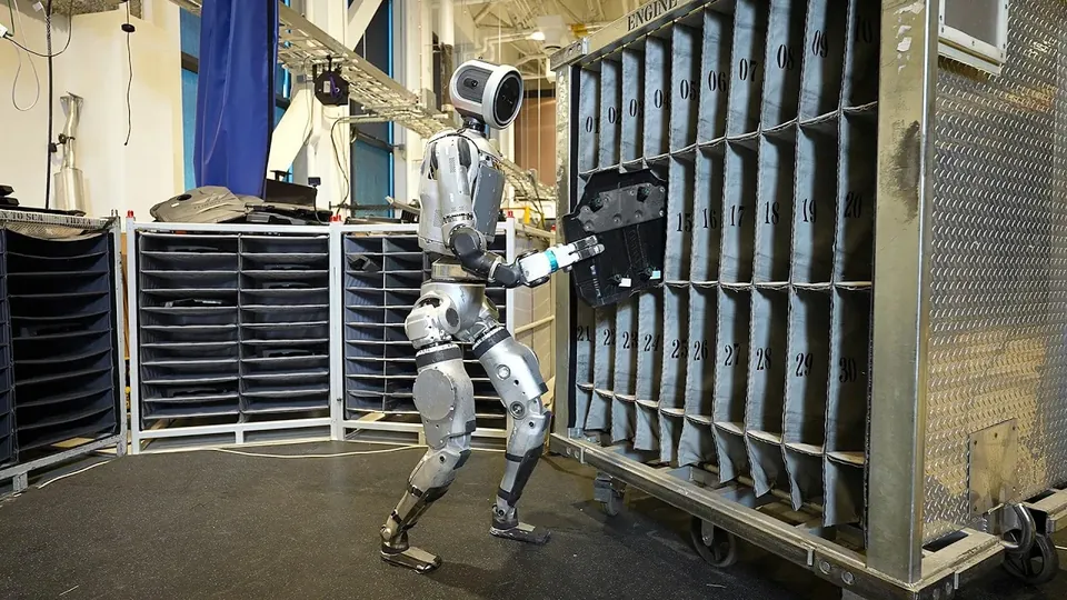 Atlas loads a part into a tall metal rack on a factory floor