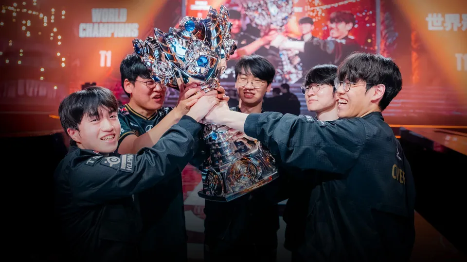 T1 players lift the Summoner's Cup together on stage in front of a World Champions screen at Worlds 2025