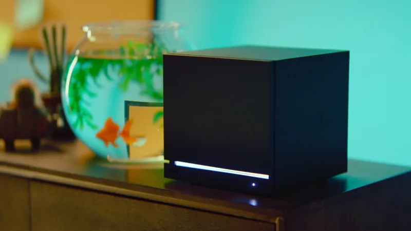 The black Steam Machine cube on a wooden cabinet next to a goldfish bowl