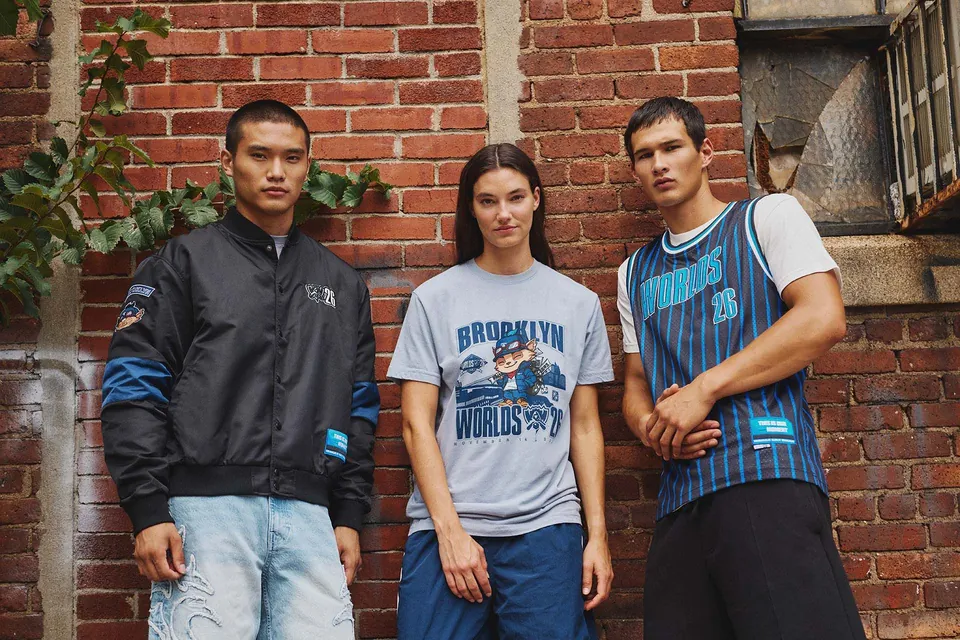 Three models in Riot's Worlds 2026 bomber jacket, Brooklyn Teemo tee and basketball jersey in front of a brick wall