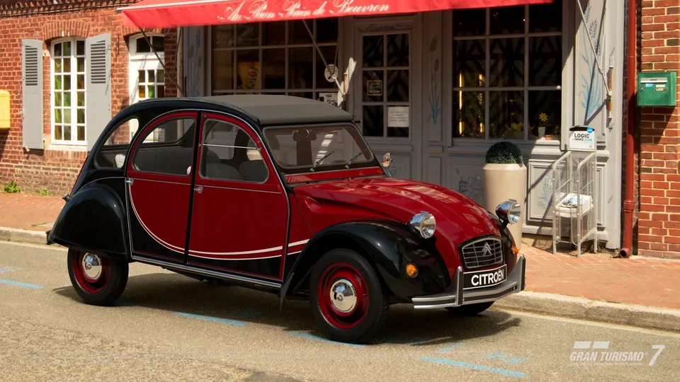 A red and black Citroën 2 CV 6 Charleston parked outside a brick café in Gran Turismo 7