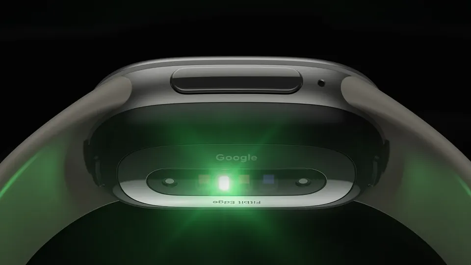 The underside of a Fitbit Edge with its health sensors glowing green against a dark background