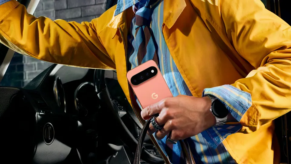 A person in a yellow jacket steps out of a car holding a Pixel 11 Pro