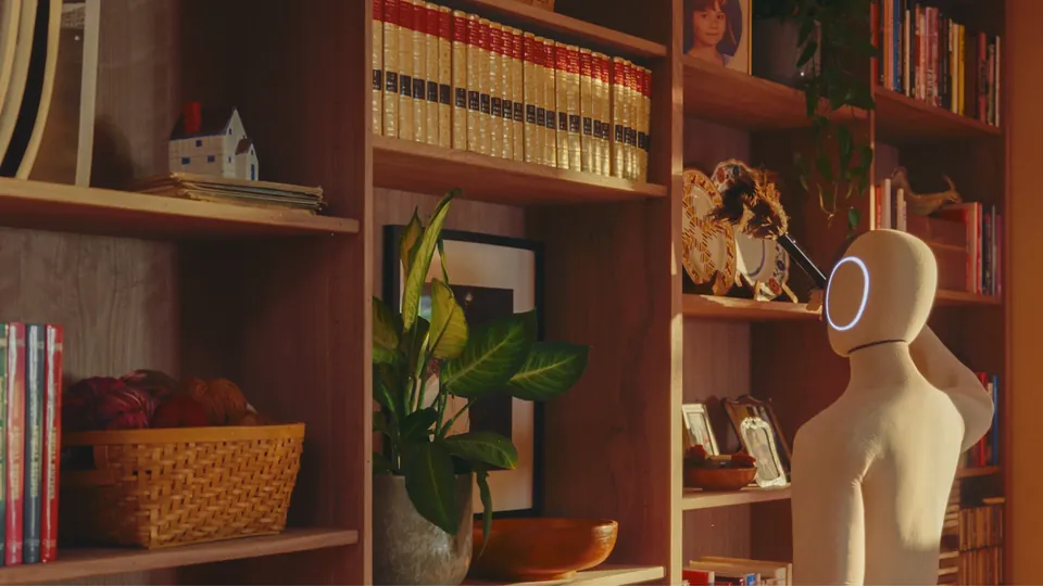 NEO stands by a bookshelf with a feather duster