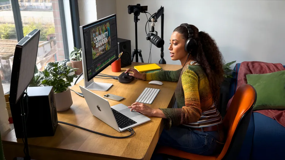 A woman records a podcast with a MacBook Pro and a microphone on her desk