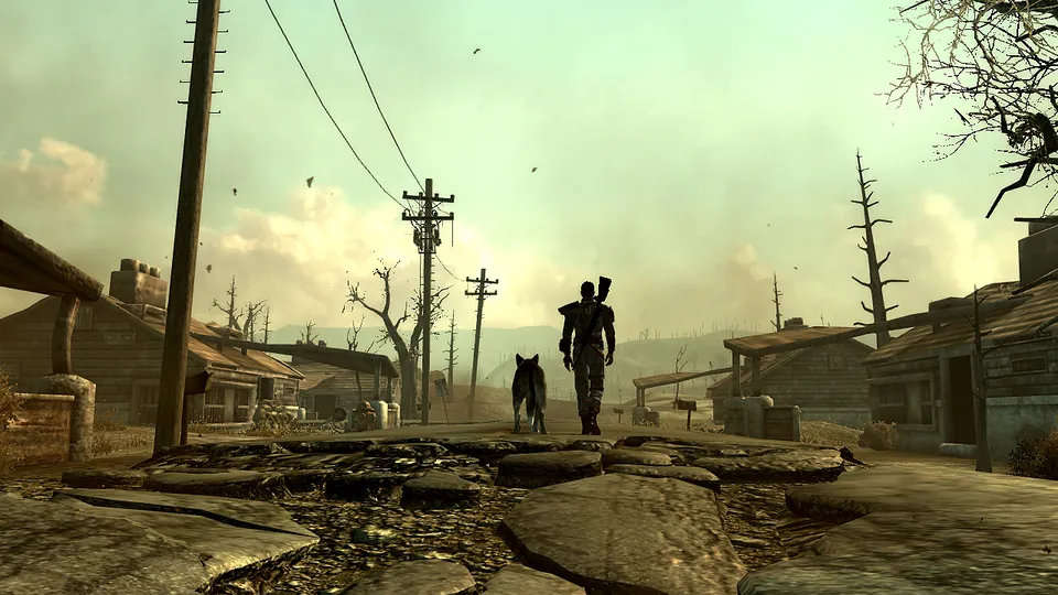 A vault dweller and Dogmeat walk down a cracked, dusty road between ruined houses and power lines in Fallout 3