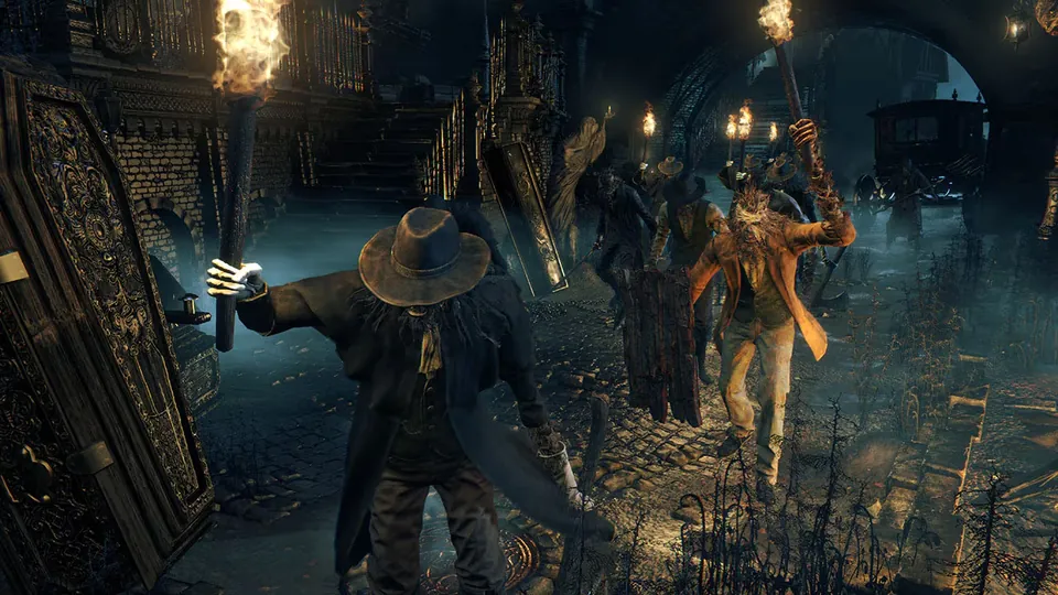 A mob of townspeople carrying torches and pitchforks gathers in a narrow cobblestone street in Bloodborne