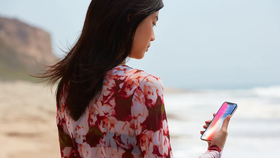 A person on a beach holds an iPhone X