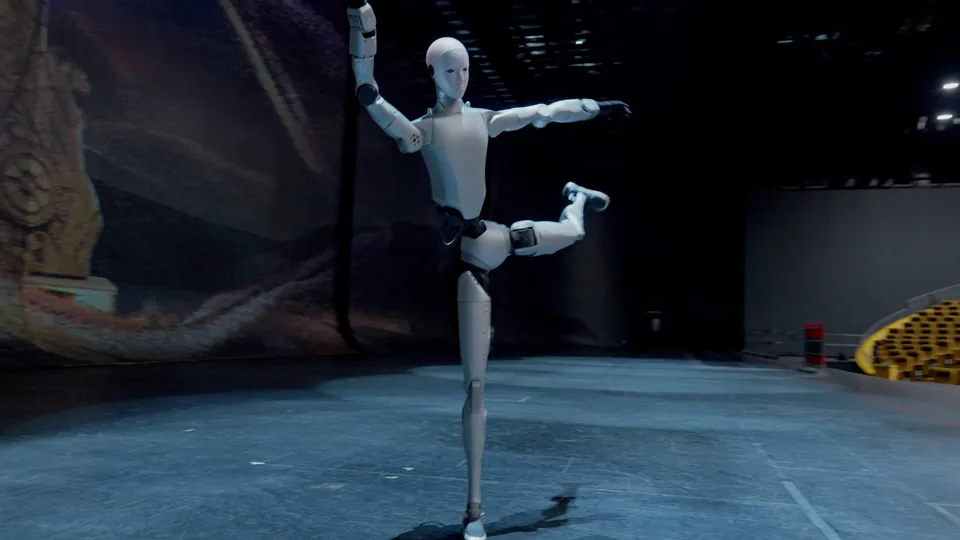 The Unitree H2 standing on one leg with its other leg raised on an empty theater stage