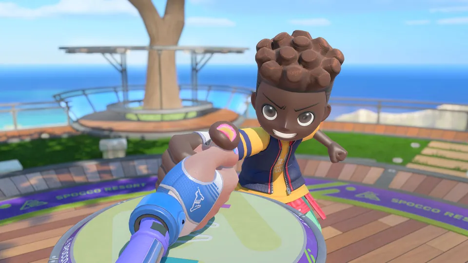 A grinning Sportsmate grips an opponent's hand in Thumb Wrestling on a deck overlooking the sea