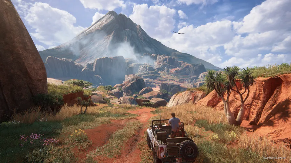 A jeep drives down a dirt road toward a mountain in Uncharted 4: A Thief's End