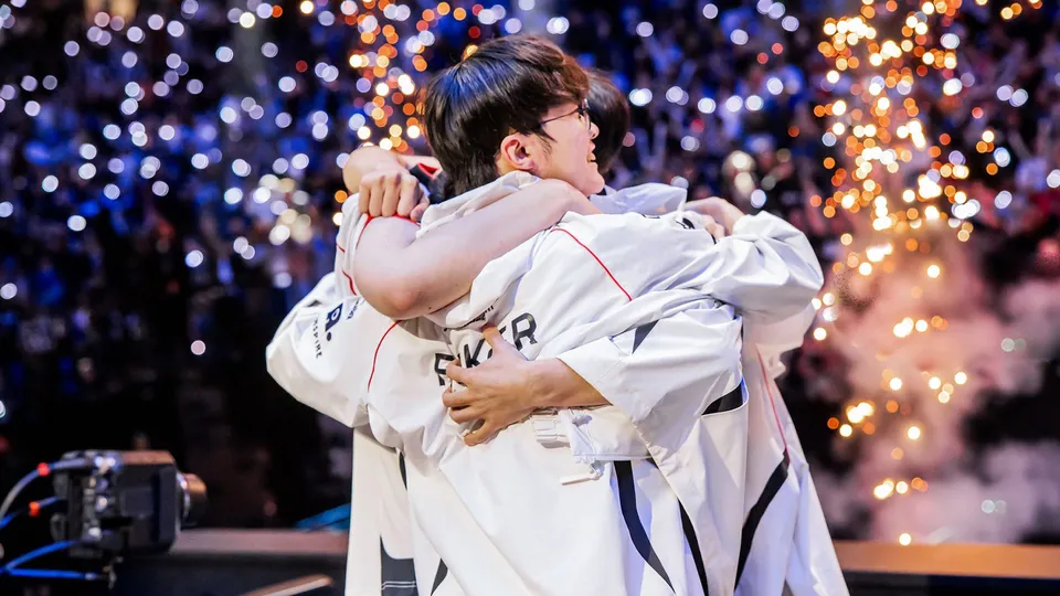T1 players in white team jackets hug on stage under fireworks, with Faker's name on the back of one jacket