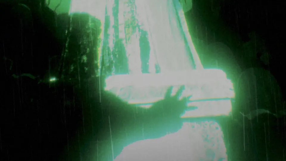 A hand reaches toward a glowing stone slab in a rainy graveyard in the Persona 6 teaser