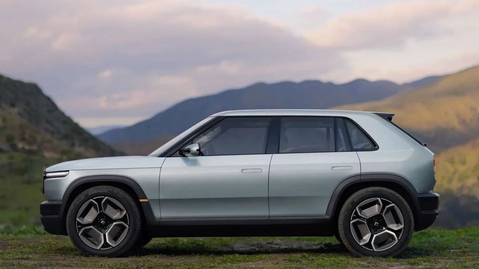A Rivian R3 in profile on a hilltop, with mountains behind it