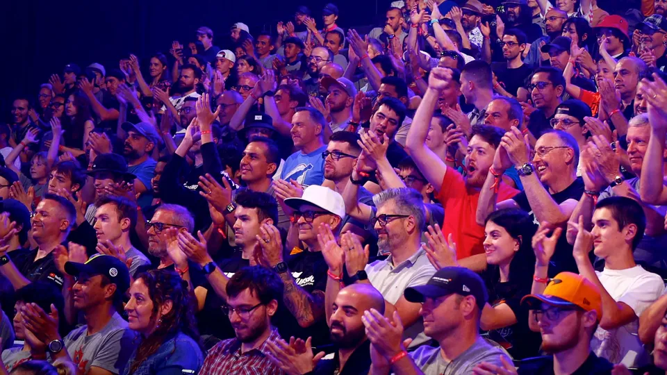 The Gran Turismo World Series stage with a giant race screen above rows of driving rigs and a crowd lit in red