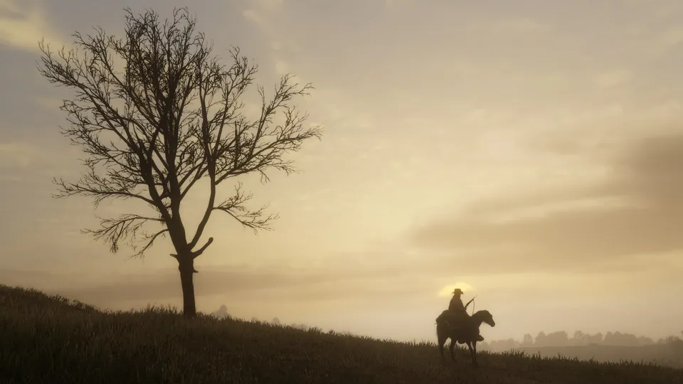 A lone rider on horseback crosses a hilltop beside a bare tree under a hazy golden sky in Red Dead Redemption 2