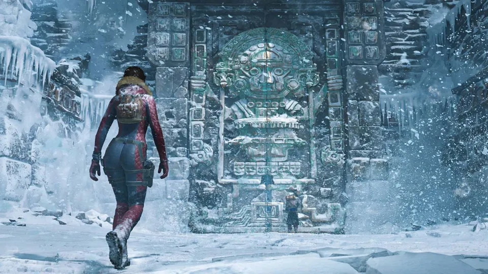 Lara Croft in a red cold-weather suit walks toward a carved stone gate in a snowstorm in Tomb Raider: Legacy of Atlantis