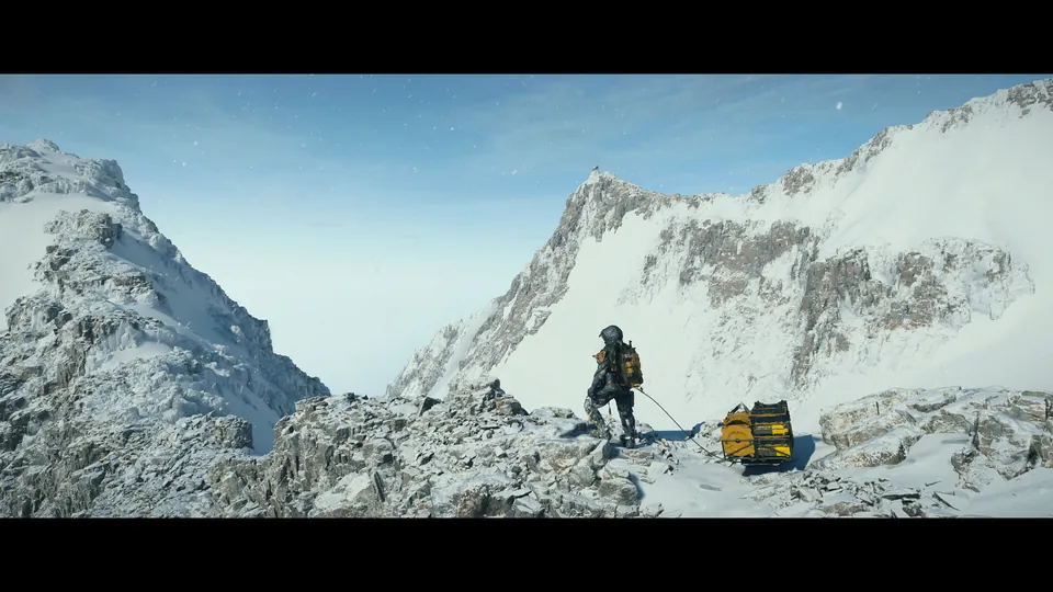 A lone porter stands on a snowy mountain ridge beside a yellow cargo case under a blue sky
