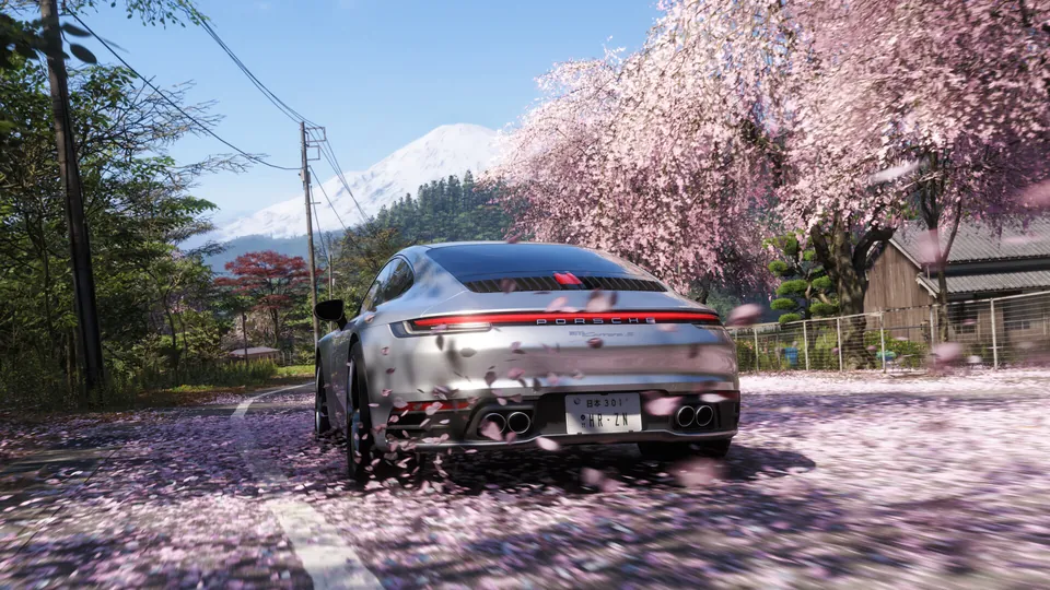 A silver Porsche 911 drives under cherry blossoms with Mount Fuji behind it