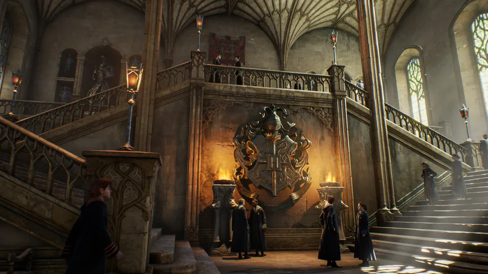 Students in black robes gather by a grand staircase and the Hogwarts crest in Hogwarts Legacy