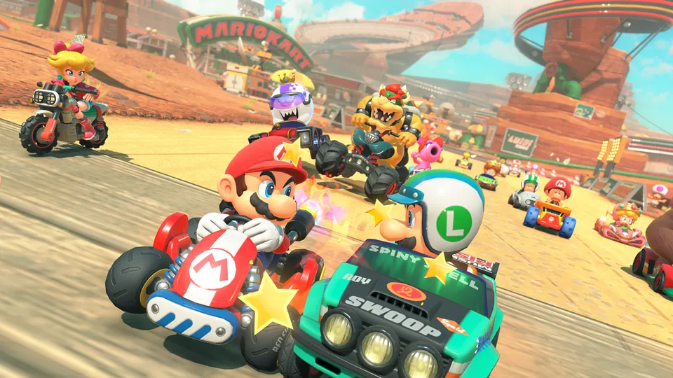 Mario leads a pack of karts and bikes driven by Luigi, Bowser, Peach and others down a sandy track in Mario Kart World